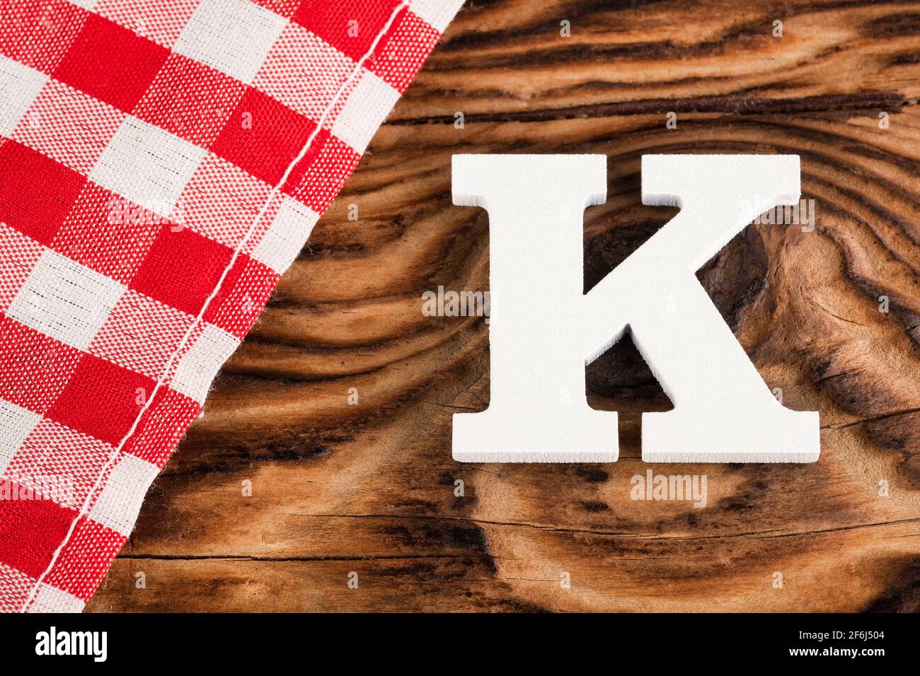Letter K of the alphabet - Red checkered cloth tablecloth on rustic wood background Stock Photo