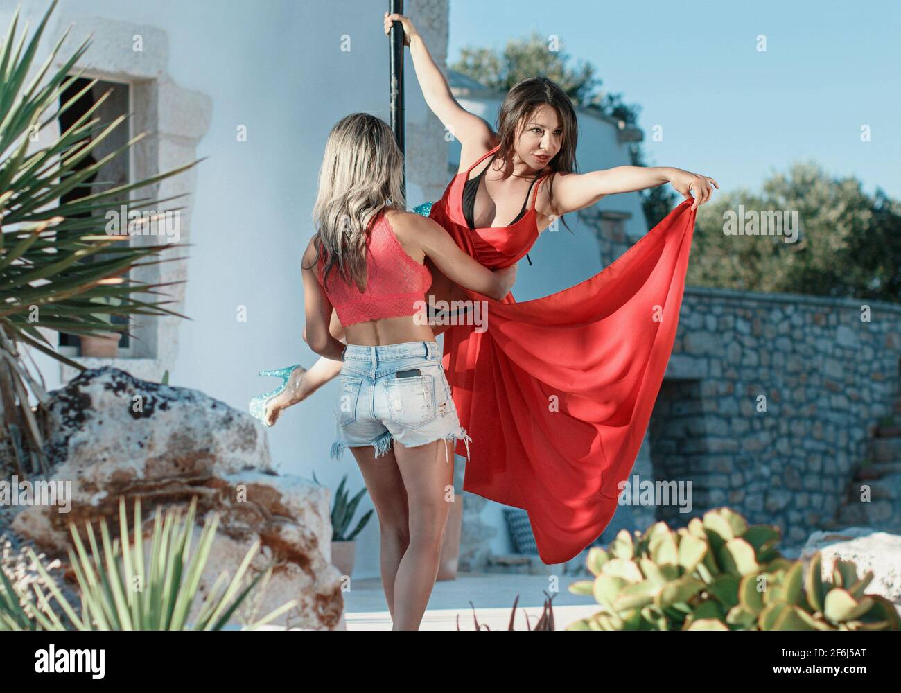 Instructor helping Young pole dancer in a dress to take a pose on a portable platform against the garden Stock Photo