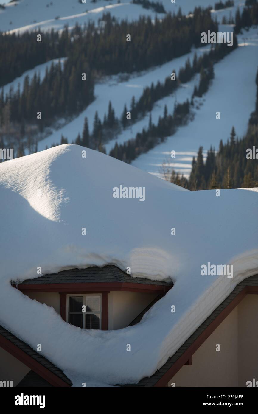 heavy snow load on roof of ski chalet at ski resort in British Columbia showing downhill ski or snowboard runs  in background of travel accommodation Stock Photo