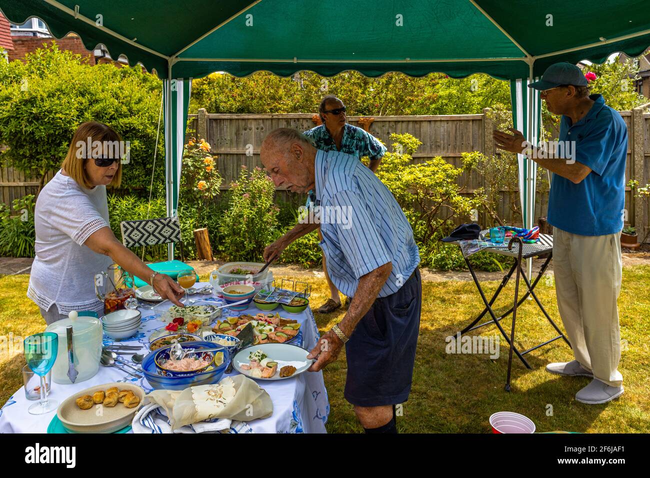 Family summer authentic garden lunch meal picnic  get together with grandpa serving himself with delicious home prepared cooked dishes, London England Stock Photo