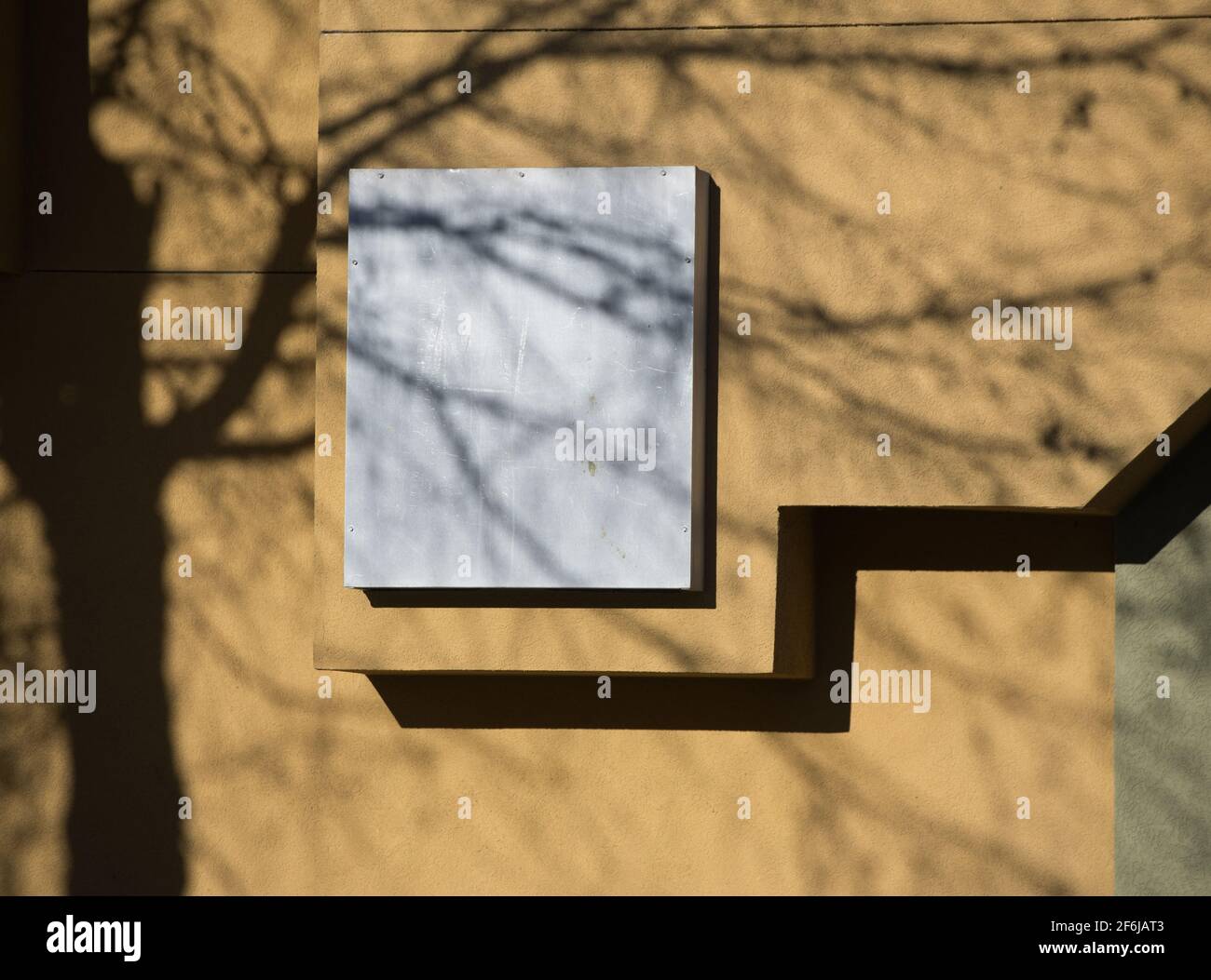 shadow of tree and branches cast on yellow concrete wall of building with architectural design grey square and zig zag line on home exterior wall Stock Photo