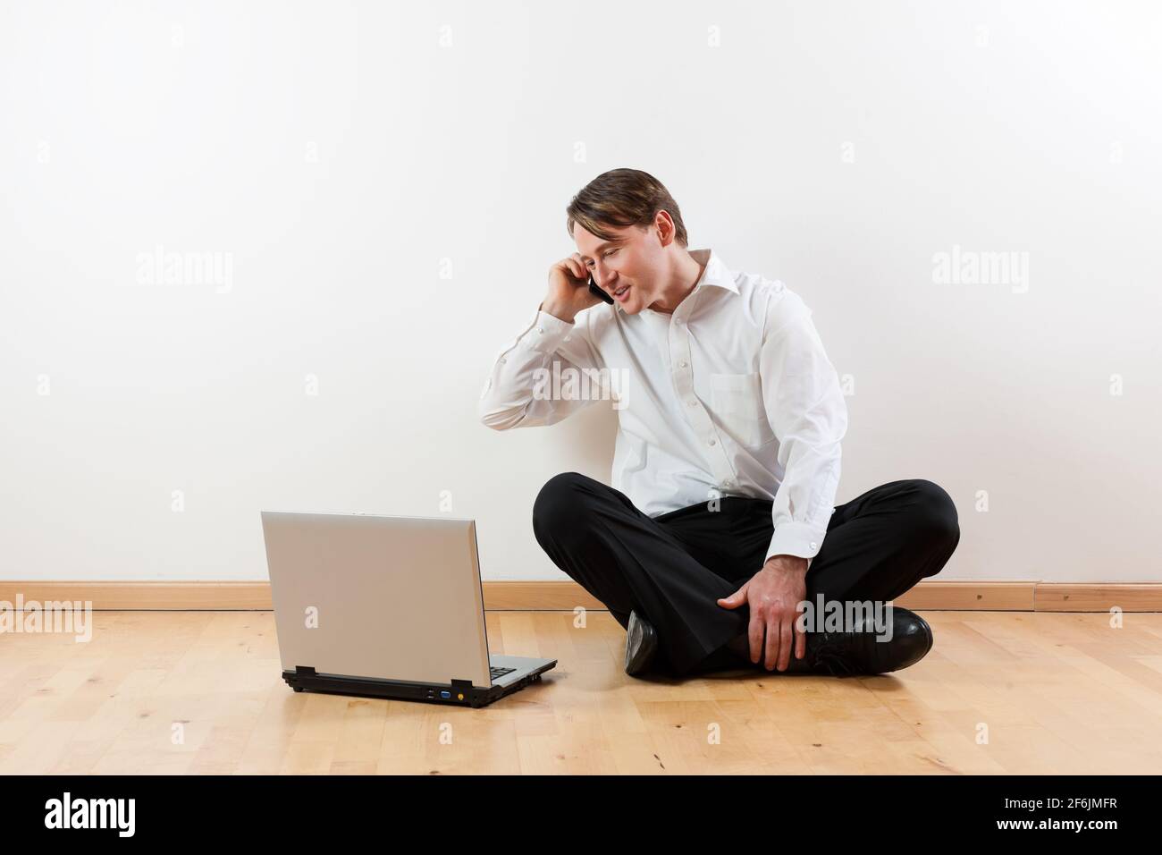 Man sitting cross-legged on the wooden floor of his apartment with ...
