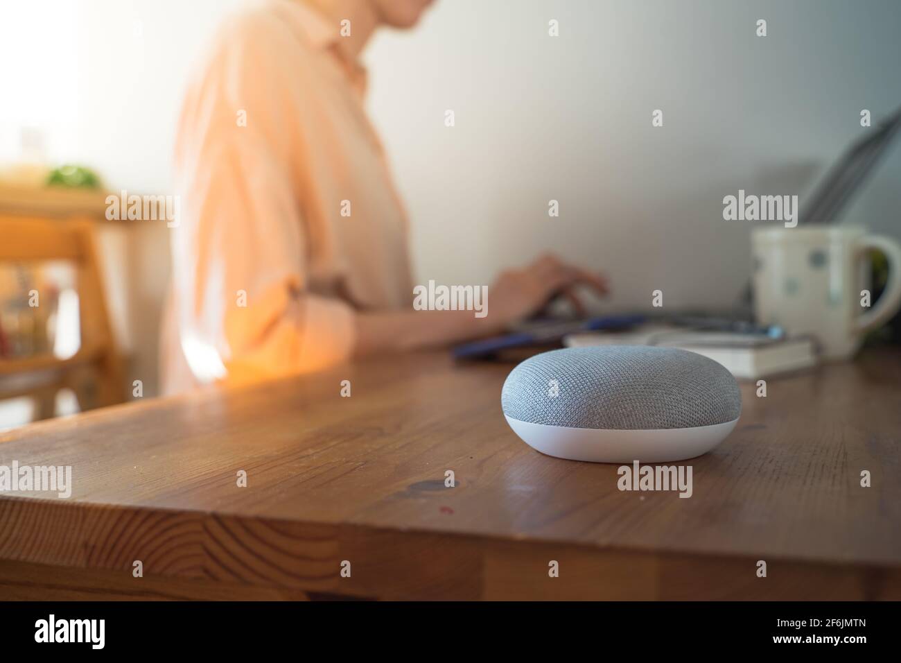 voice controlled smart speaker with a woman in the background in a interior home environment. Stock Photo