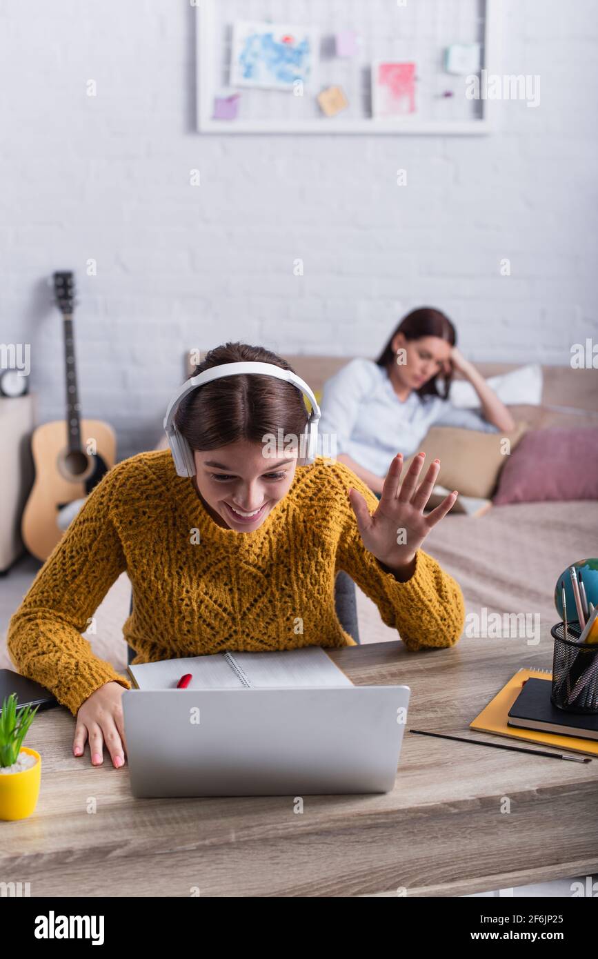happy teenage girl in wireless headphones waving hand while having ...