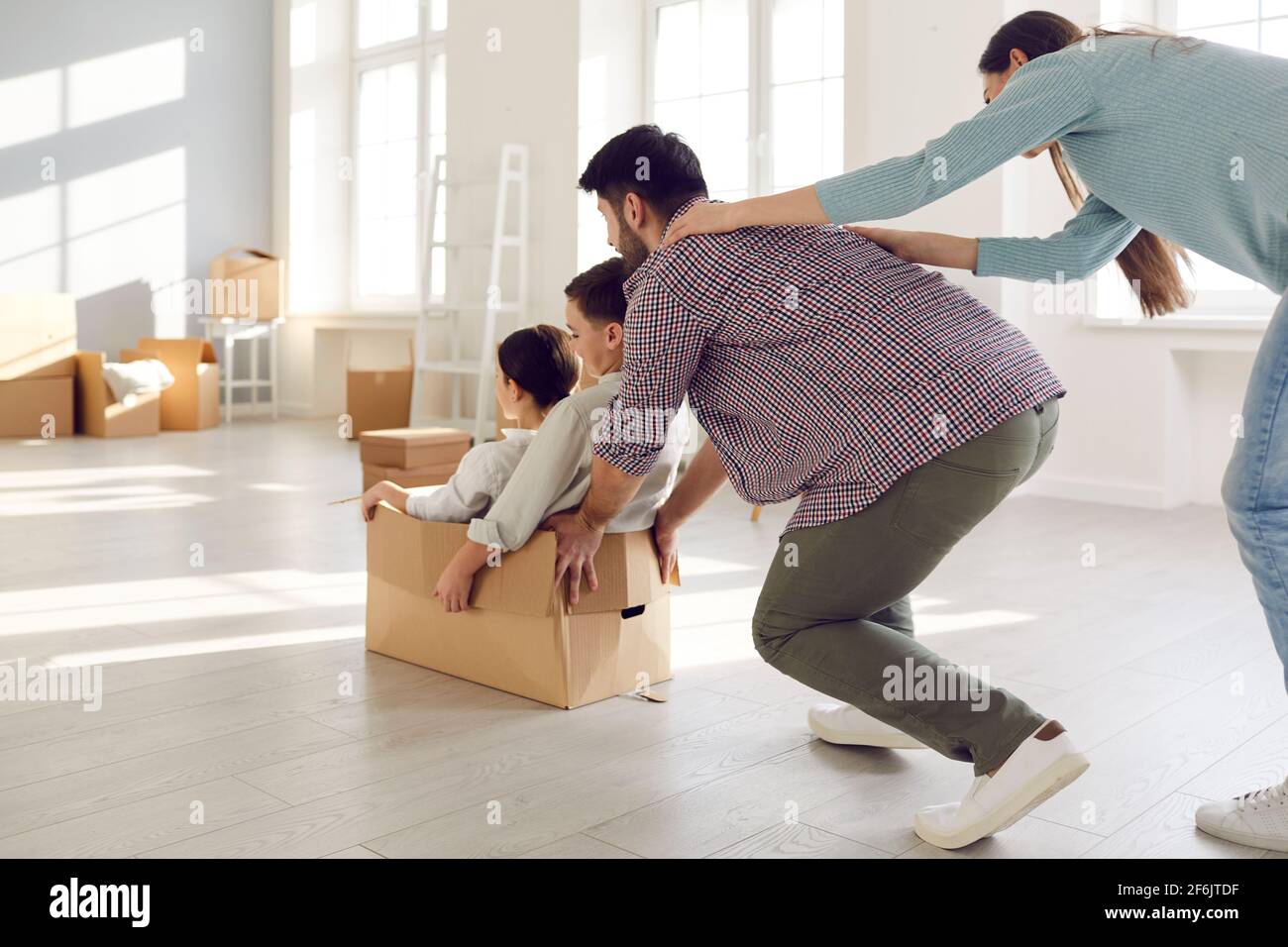 Rear view on overjoyed parents riding kids in cardboard box on moving day Stock Photo