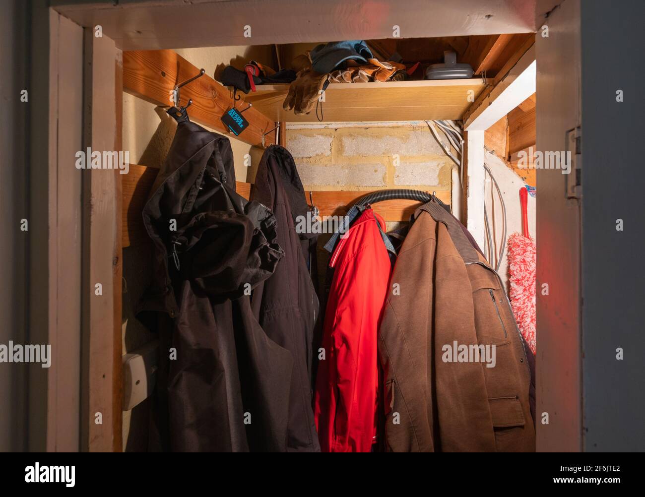Coats hanging up in a small cupboard or closet under the stairs, where you can hang a coat and store other items, in a British home in England, UK. Stock Photo