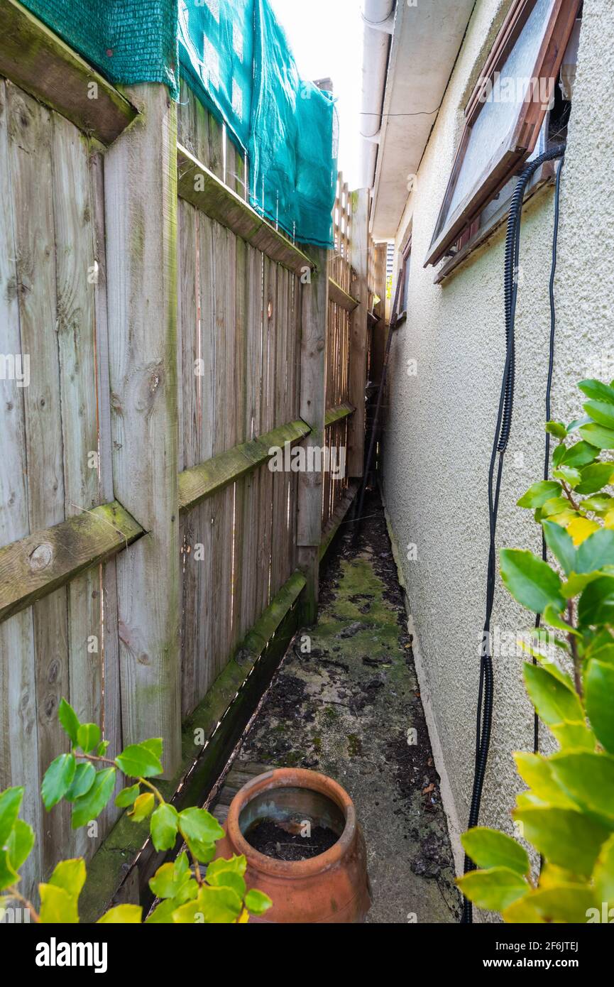 Narrow gap, an ideal hiding place between a wooden garden fence and a garage. A great place to hide for animals such as cats, dogs and foxes. Stock Photo