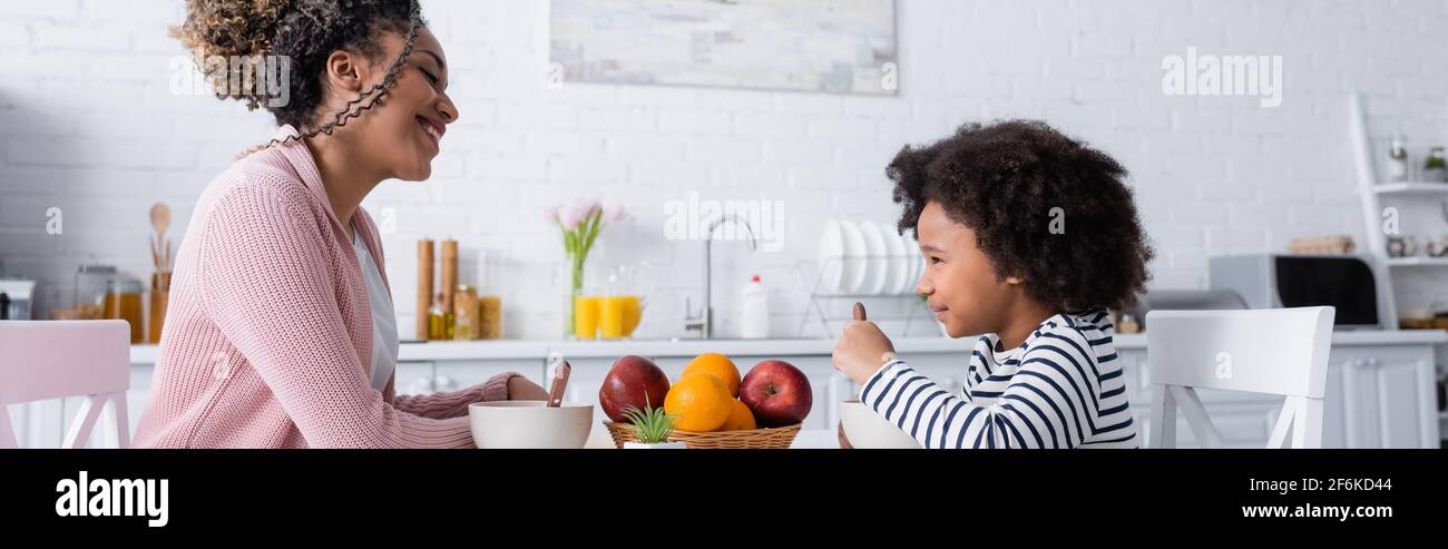 happy african american mom and daughter looking at each other during breakfast, banner Stock Photo