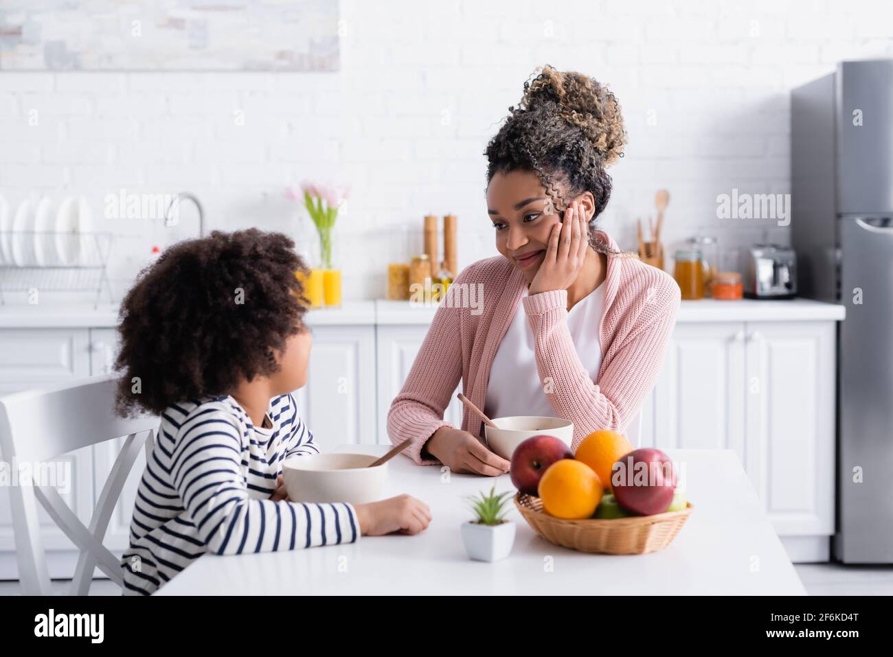 smiling african american woman looking at daughter during breakfast in kitchen Stock Photo