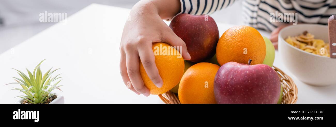 cropped view of african american kid taking orange from wicker basket with fresh fruits, banner Stock Photo