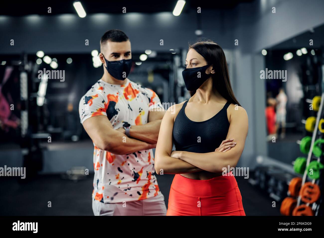 Muscular couple standing in gym with arms crossed with face masks during corona virus. Prevention from corona virus, fitness, healthy life Stock Photo