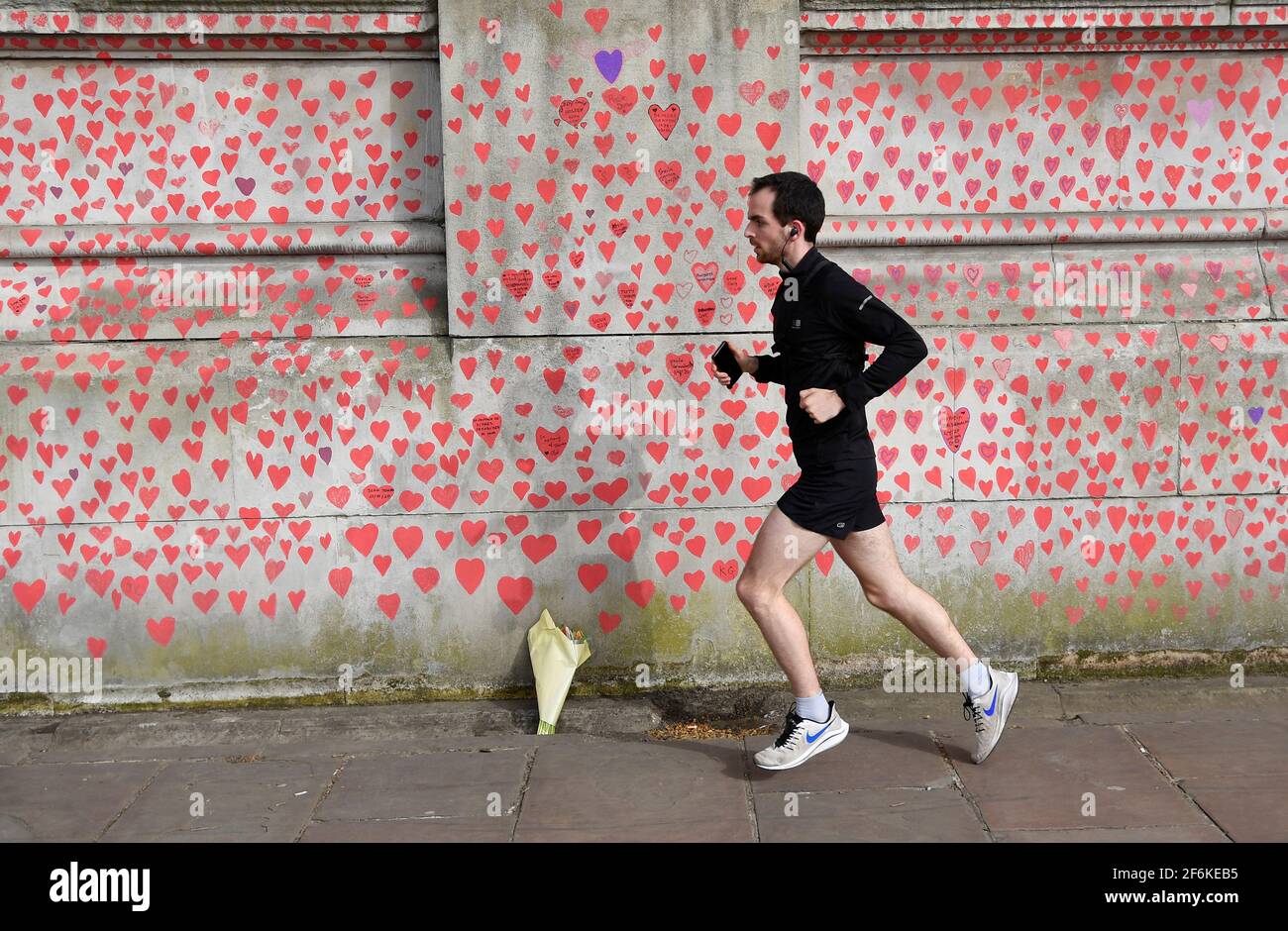 A man runs past a wall of hearts being painted by volunteers and relatives of bereaved beside St Thomas' hospital as a memorial to all those who have died so far in the UK from COVID-19, amid the spread of the coronavirus disease (COVID-19) pandemic in London, Britain, April 1, 2021. REUTERS/Toby Melville Stock Photo