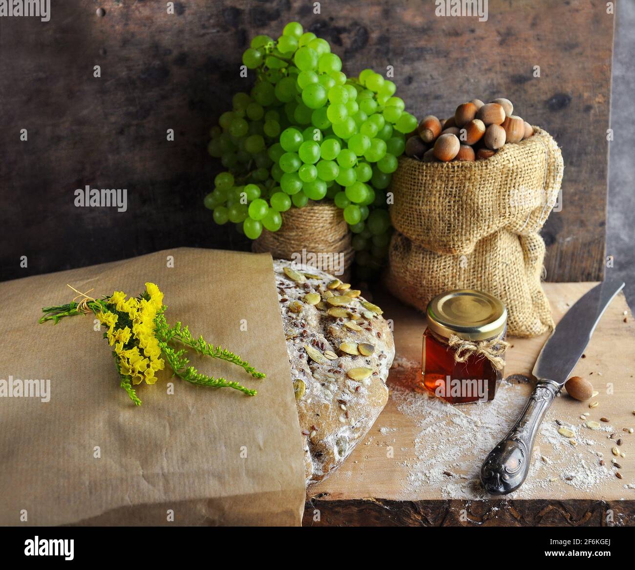 Rustic style bread with a bunch of grapes, nuts in a bag, honey, a knife. Stock Photo