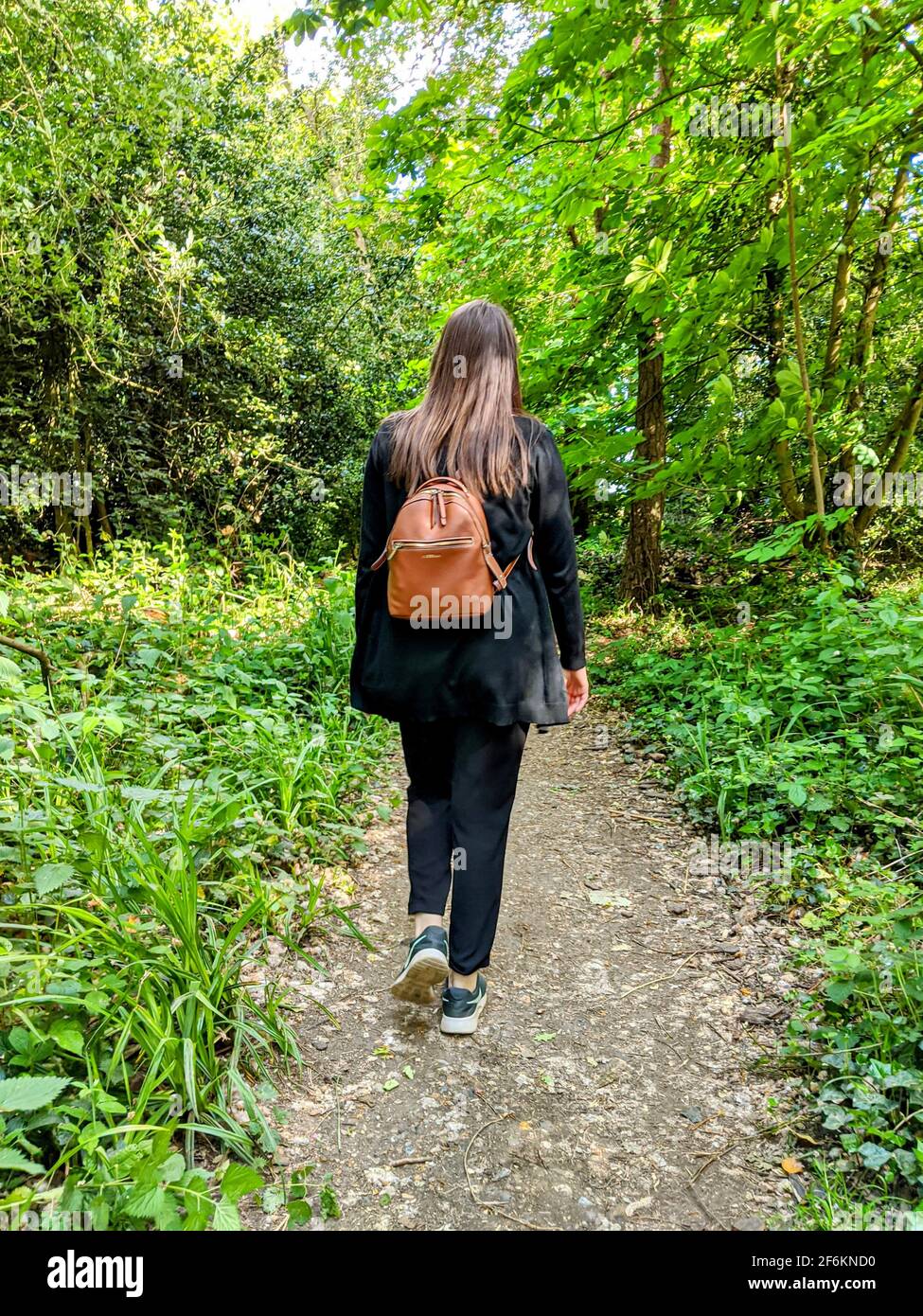 A brunette woman walking away down a woodland path surrounded by green shrubbery, bushes and trees on Hampstead Heath, London, U.K. Stock Photo