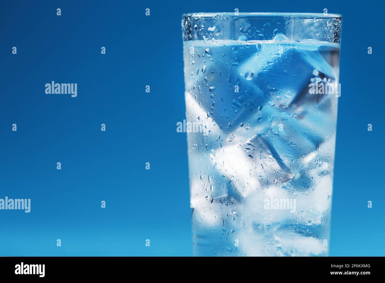 A glass with ice water and ice cubes on a blue background. A refreshing ...