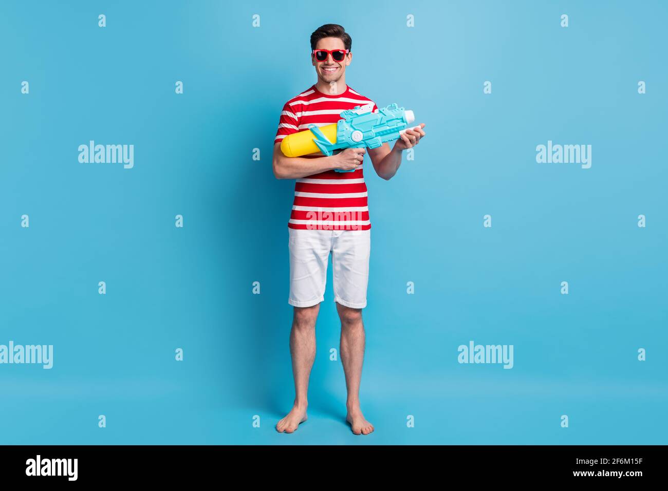 Full length body photo happy man holding water gun playing on the beach isolated on vivid blue color background Stock Photo