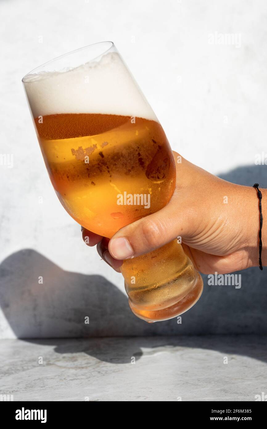 Hand holding a glass with frothy IPA beer on a hot day Stock Photo