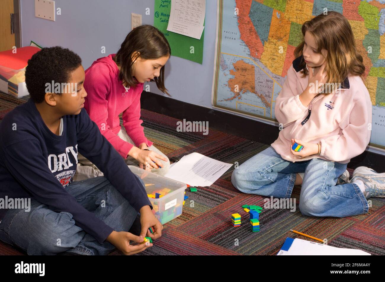 independent elementary school Grade 4 ages 9-10 mathematics group of two girls and a boy working together problems using math manipulatives Stock Photo