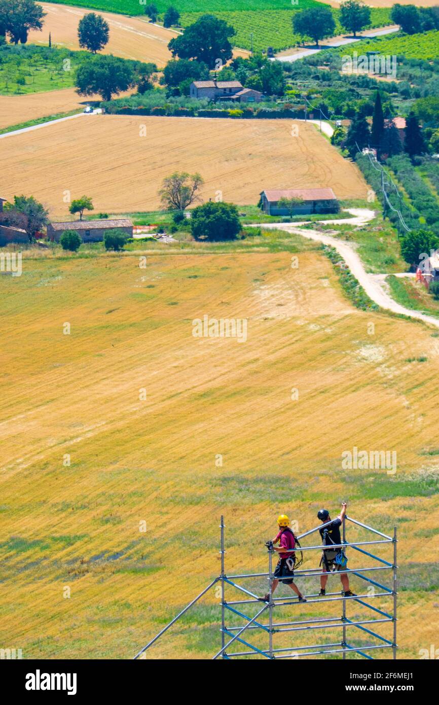 Two workers work on a scaffolding, behind the plain of Spoleto, seen from Assisi Stock Photo