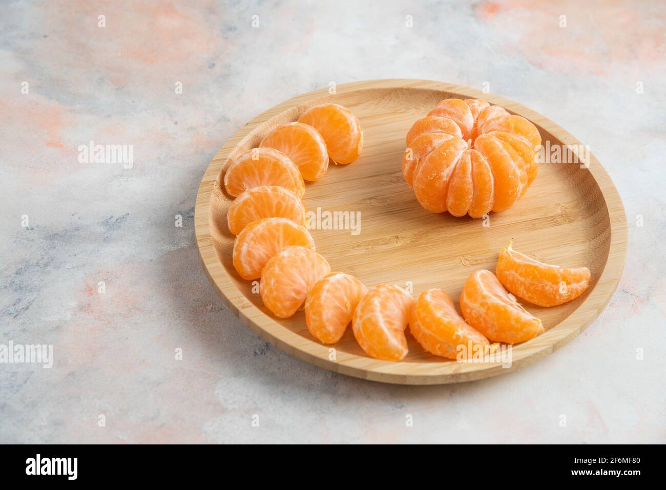 Peeled clementine mandarins over wooden plate on background Stock Photo