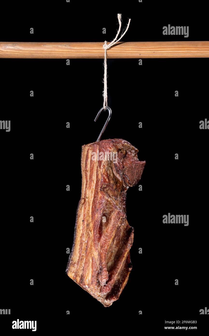 Delicious smoked bacon hung on a string. Meats prepared according to the home recipe. Dark background. Stock Photo