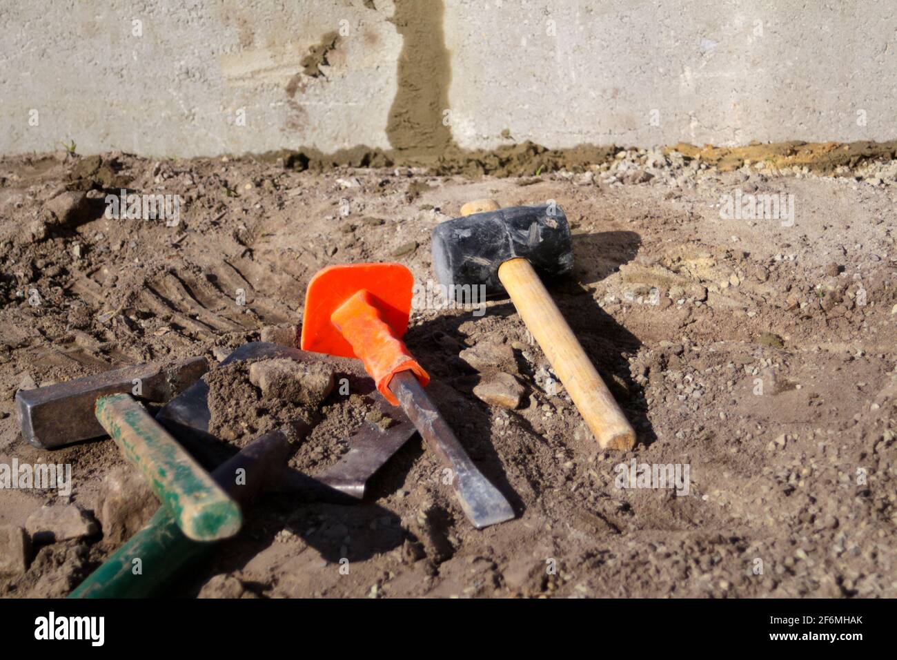 Defocus hammer, mallet, chisel and bayonet of the shovel lie on the ground. Set of tools for laying paving stones. Preparing to lay patio with stone. Stock Photo