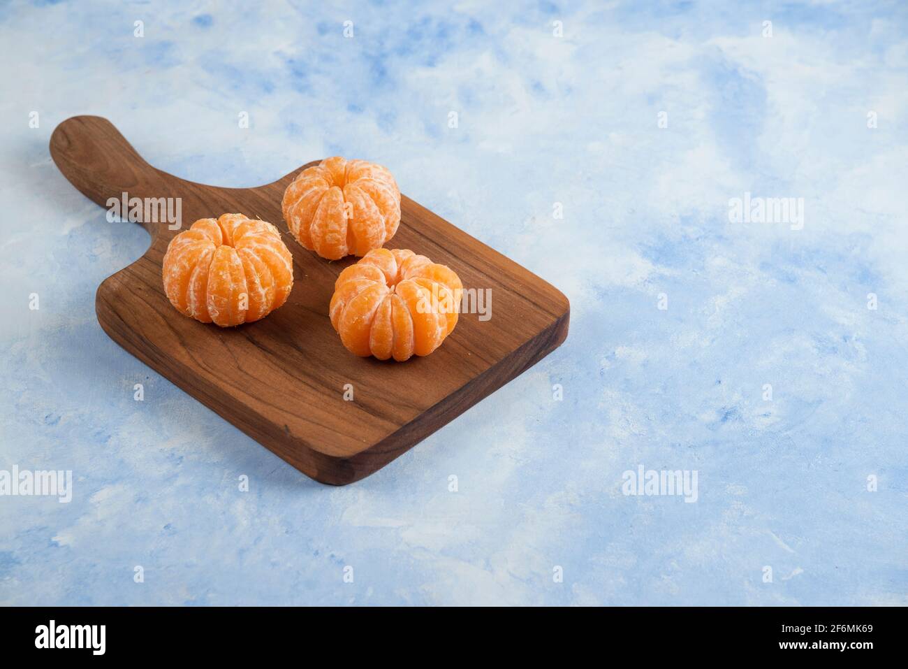 Three fresh peeled mandarin on wooden cutting board. Close up photo Stock Photo