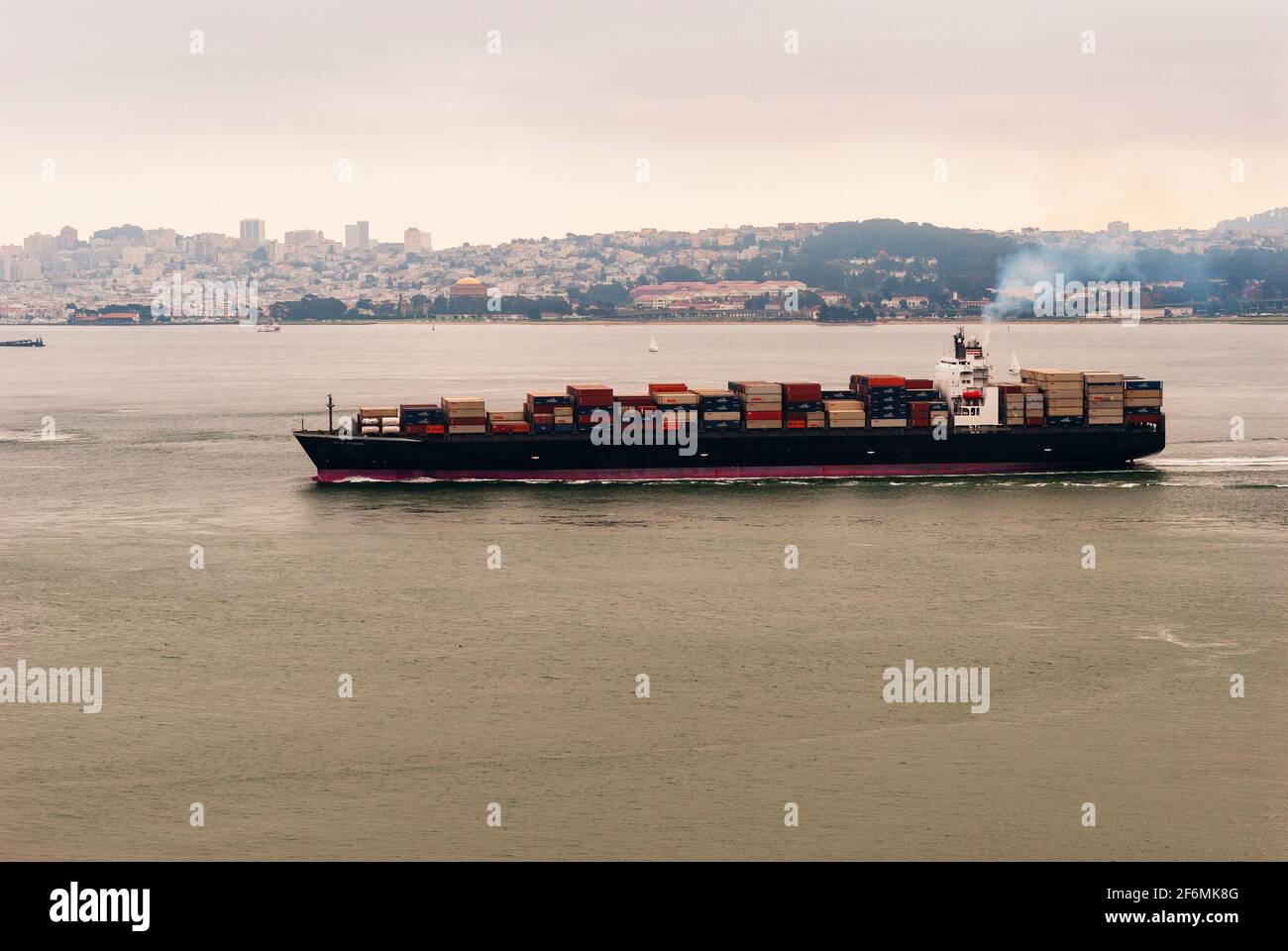A container barge carrying goods sails in San Francisco bay with San Francisco in the background. California, USA. Stock Photo