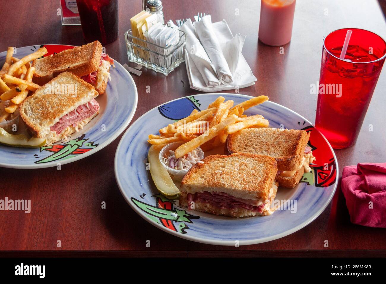 Two plates with Reuben sandwiches, dill pickle, cole slaw or coleslaw, with french fries or chips, with drinks. Stock Photo