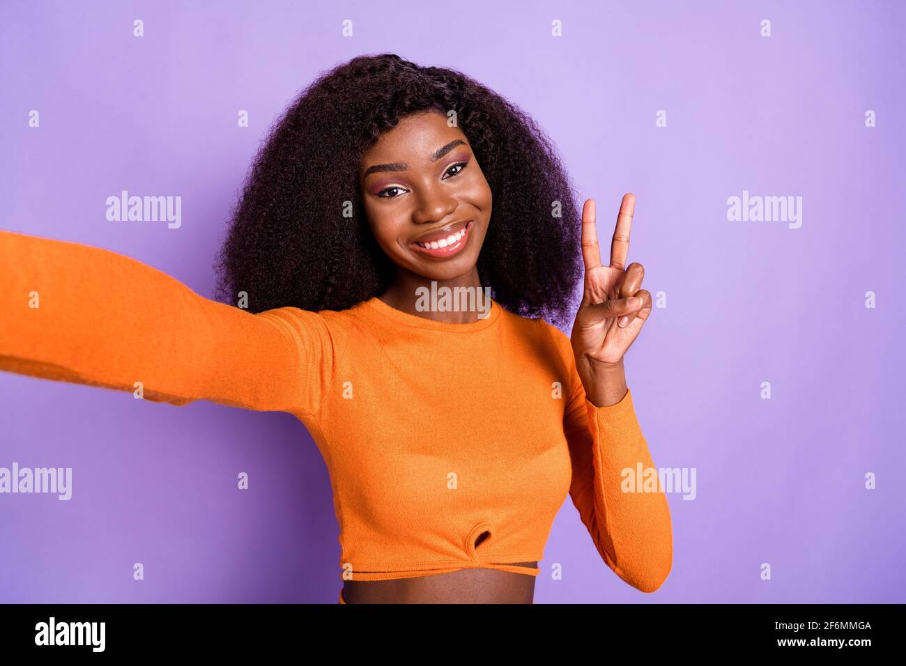Photo of funny cute dark skin woman dressed orange shirt tacking selfie  showing v-sign isolated purple color background Stock Photo - Alamy, image size:1300x956