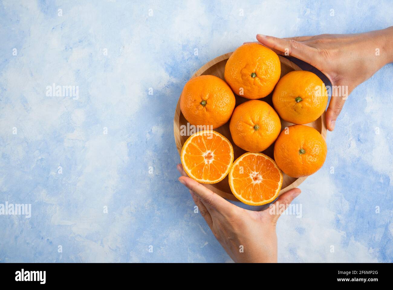 Female hand taking slice from pile. Clementine mandarins on blue background Stock Photo