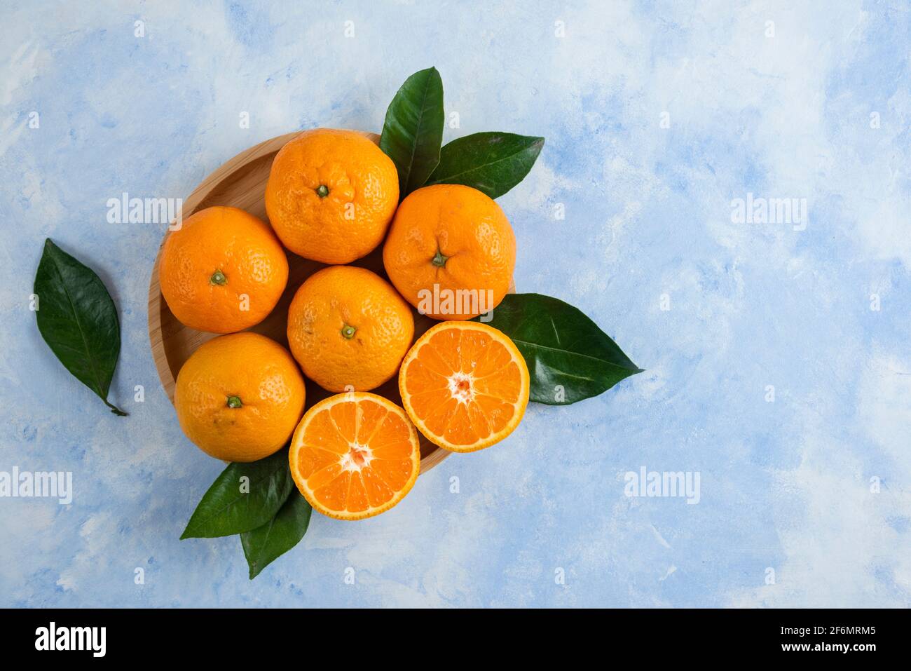 Top view of clementine mandarins with leaves on wooden plate Stock Photo