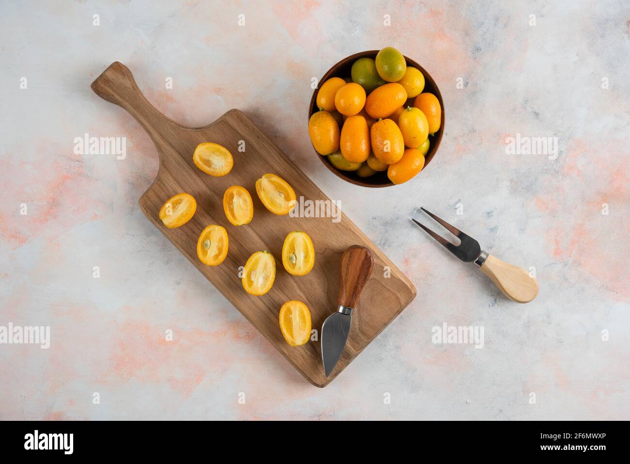 Whole kumquats in bowl and half cut kumquats on wooden cutting board Stock Photo