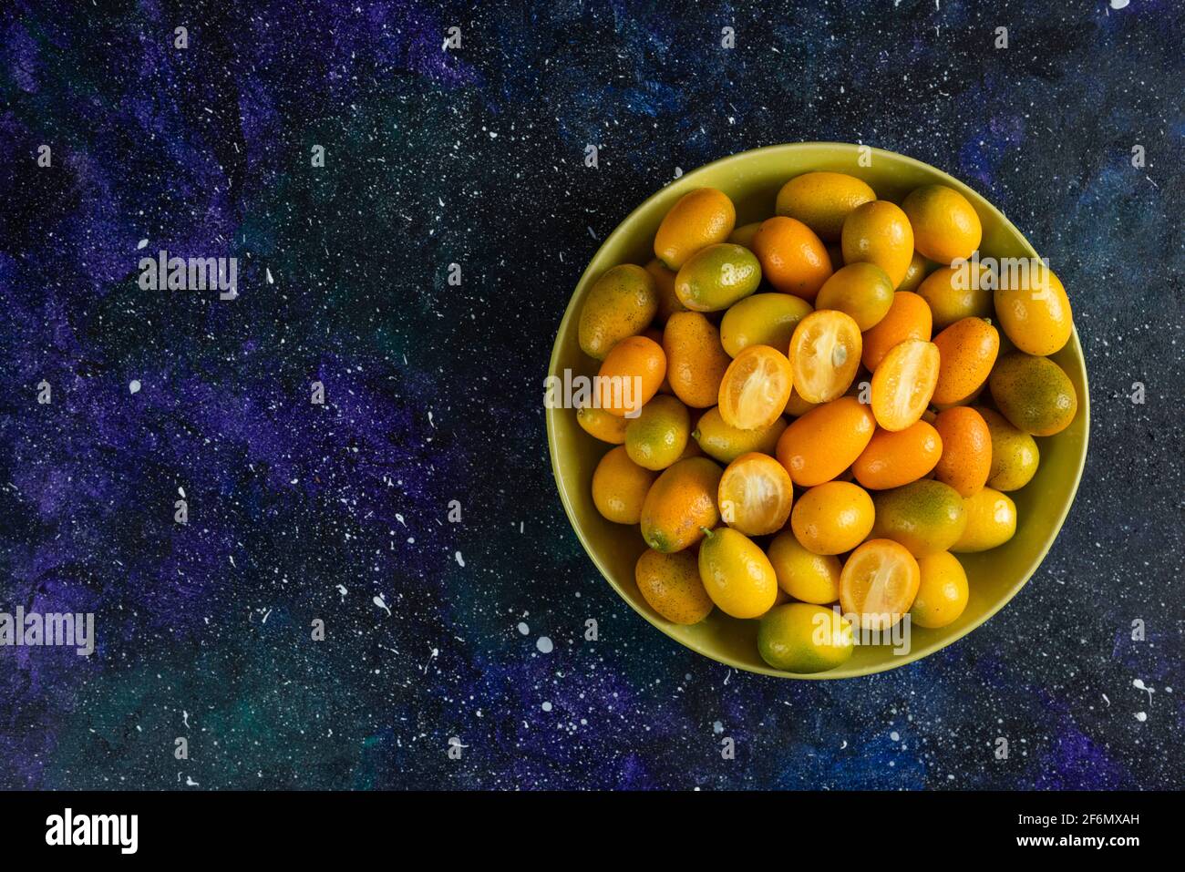 Pile of kumquats in ceramic bowl over blue background Stock Photo