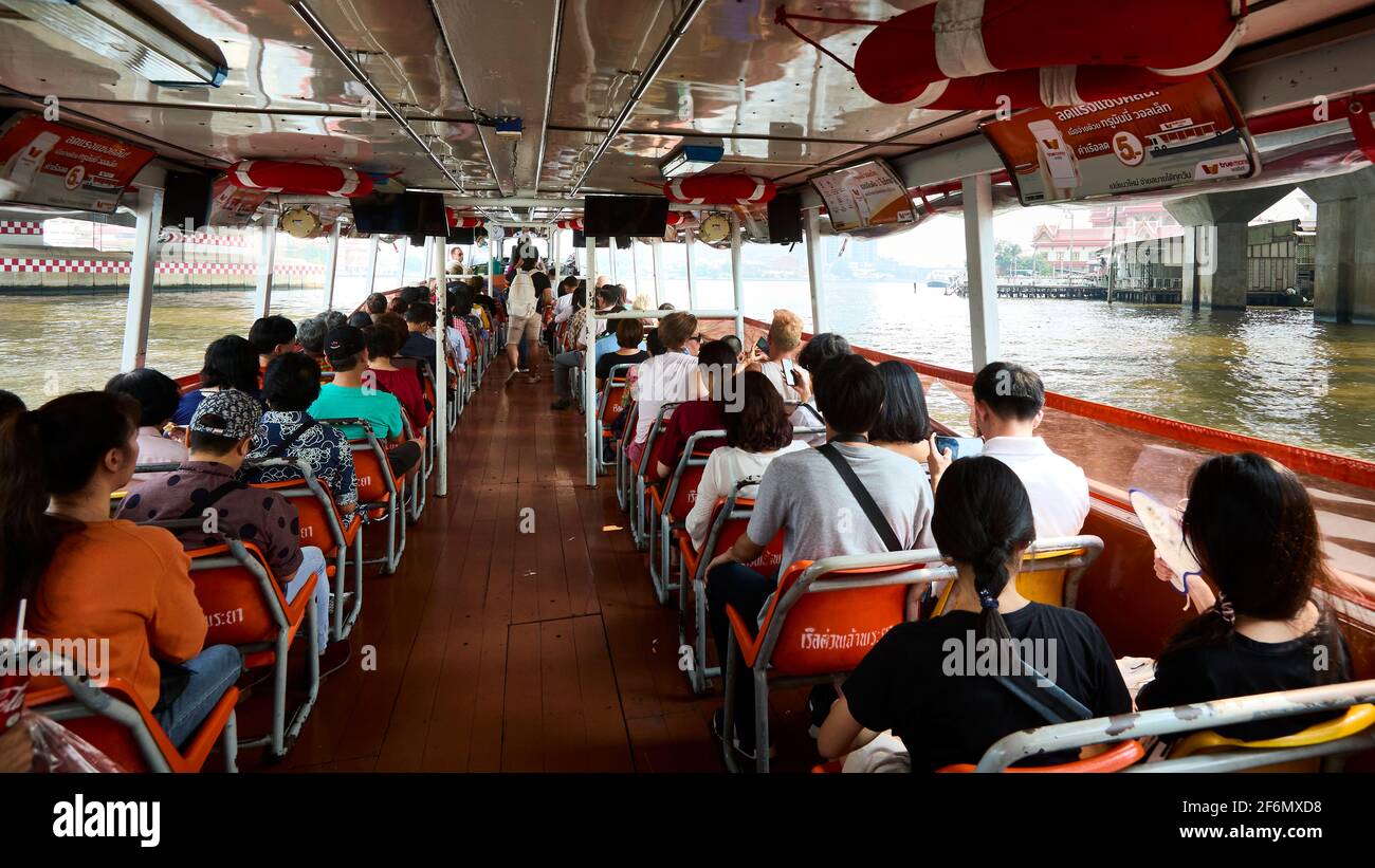 Thai locals and tourists riding to their destinations on a long boat in Thailand on the Chao Phraya River in the afternoon Stock Photo