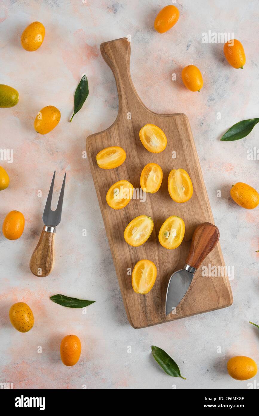 Pile of kumquats, Whole or half cut on wooden cutting board. Vertical photo Stock Photo