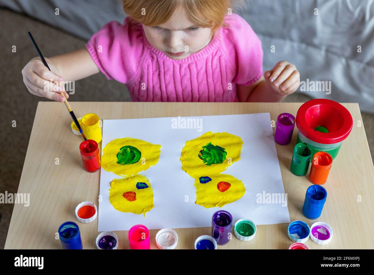 Little smiling girl painting on paper with colorful paints sitting at the table at home Stock Photo