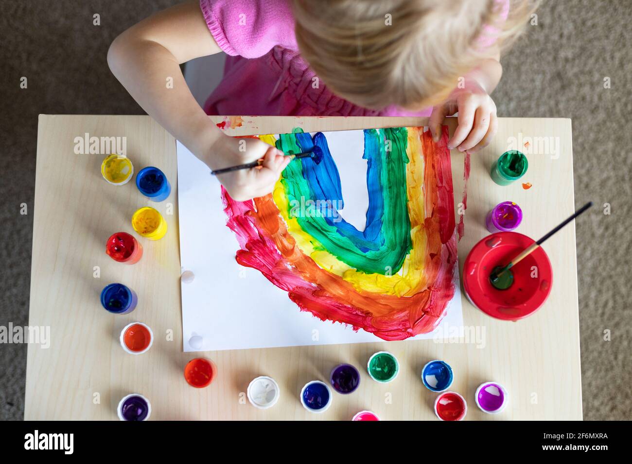 Little girl painting rainbow on paper with colorful paints sitting at the table at home Stock Photo