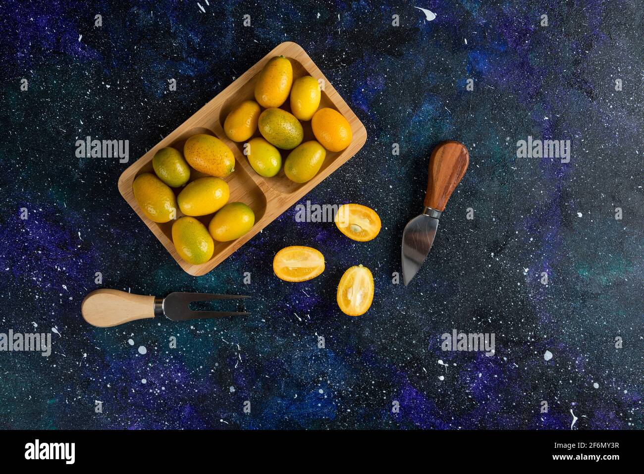 Pile of kumquats on wooden plate whole or half cut Stock Photo