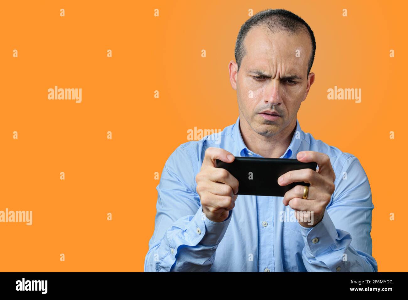 Mature man in formal wear looking at his smartphone and very sad. Orange background. Stock Photo