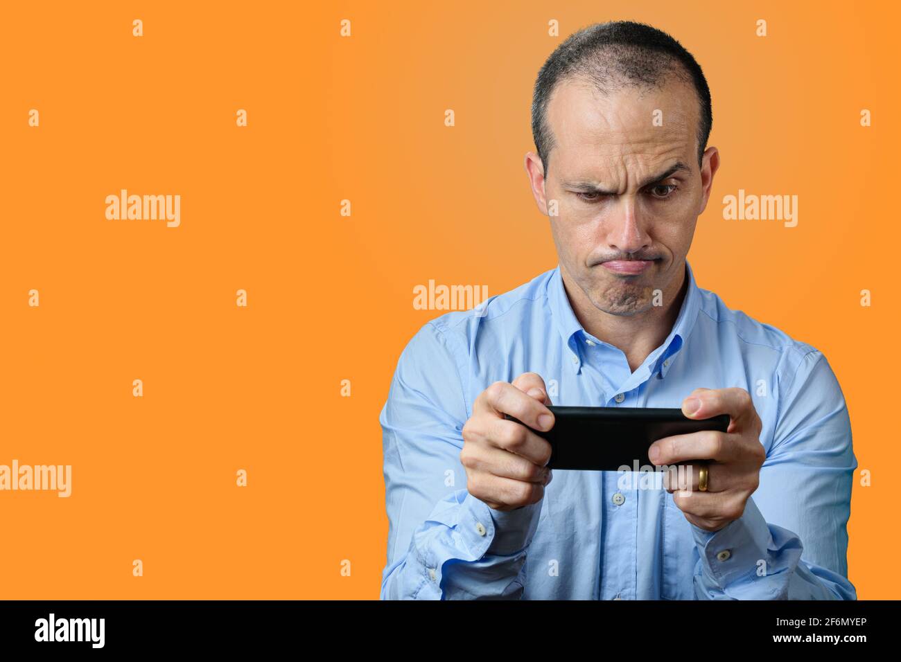 Mature man in formal wear looking at his smartphone and biting his upper lip. Orange background. Stock Photo