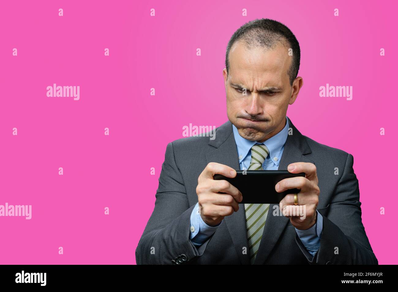 Mature man with suit and tie, playing on his smartphone and breathing through his nose. Pink background. Stock Photo