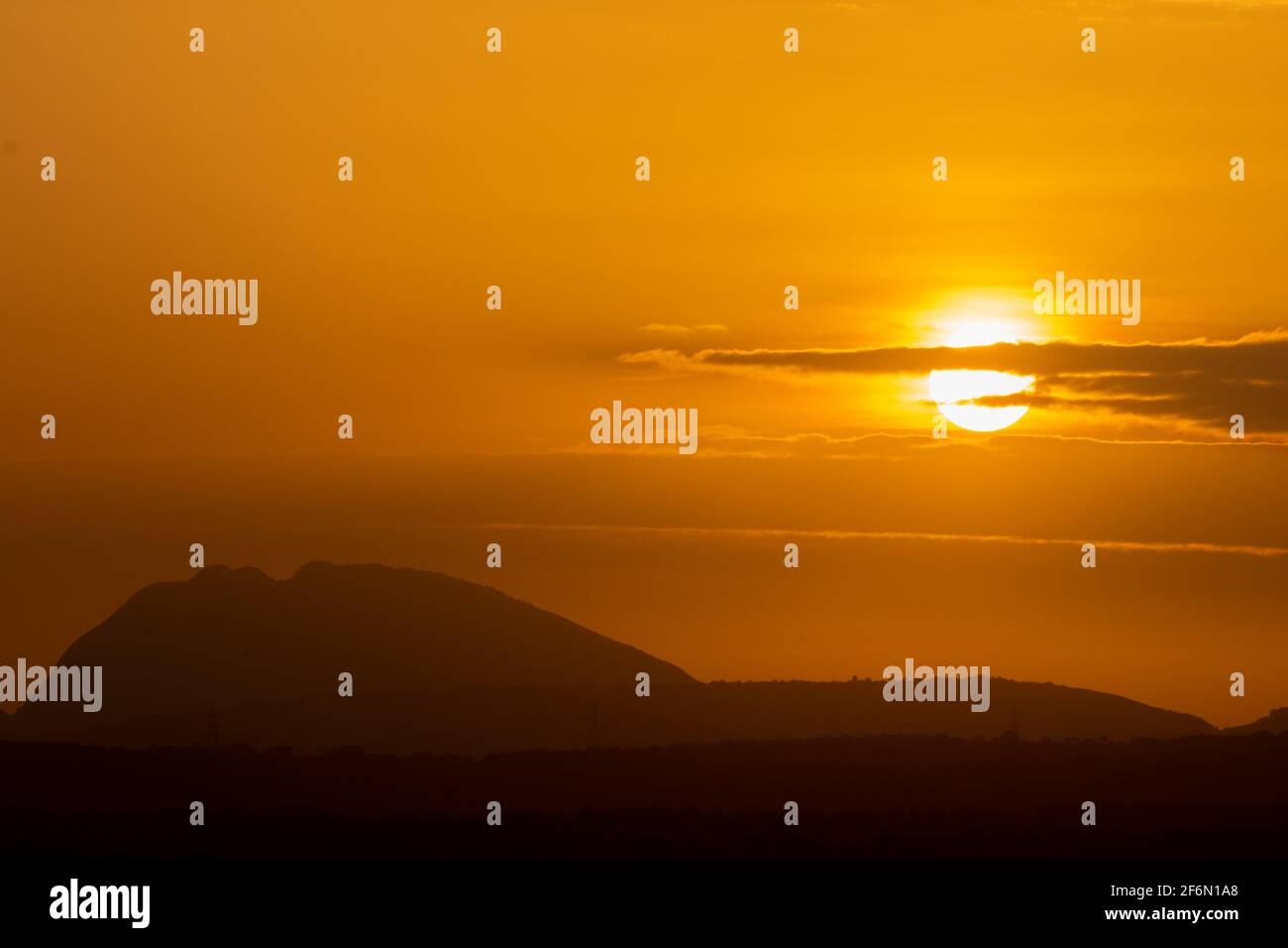 Silhouette of hills against beautiful golden hour sunset amidst a streak of clouds and beautiful orange sky Stock Photo