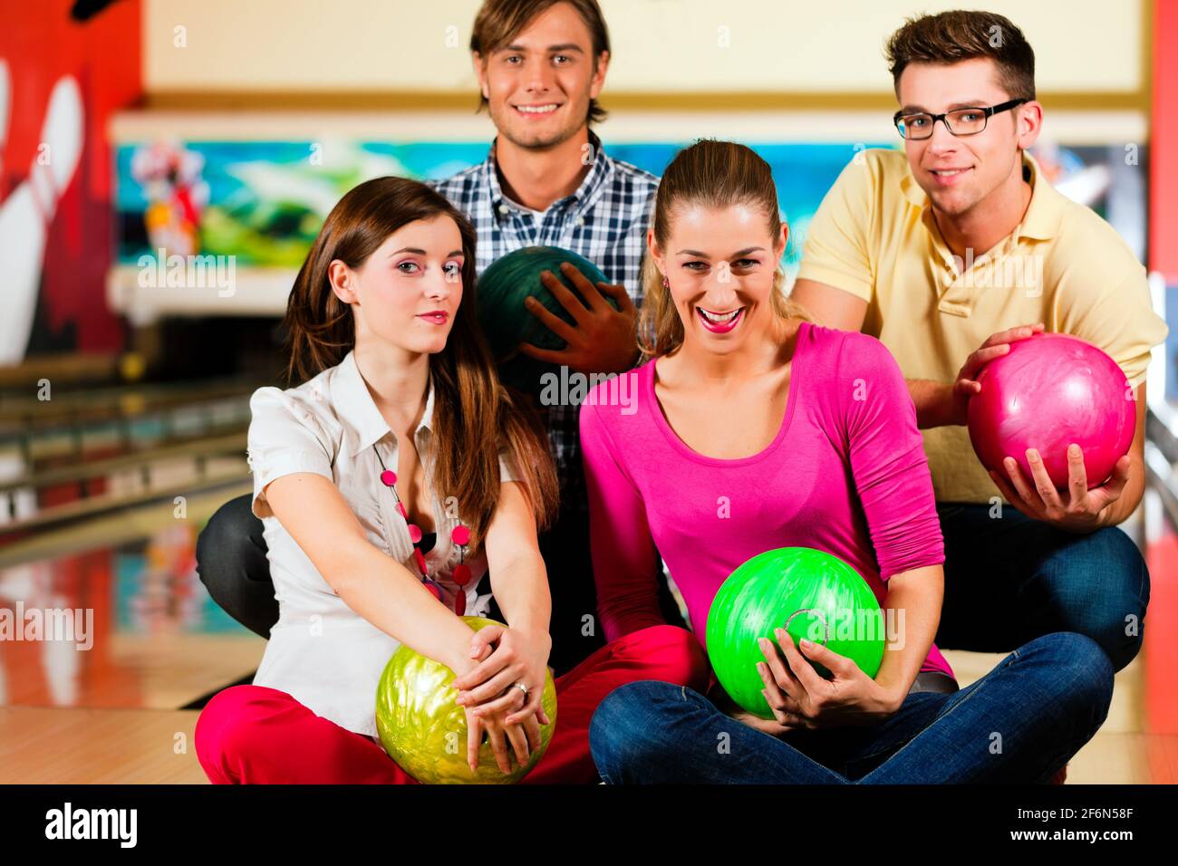 Group of four friends in a bowling alley having fun, holding their