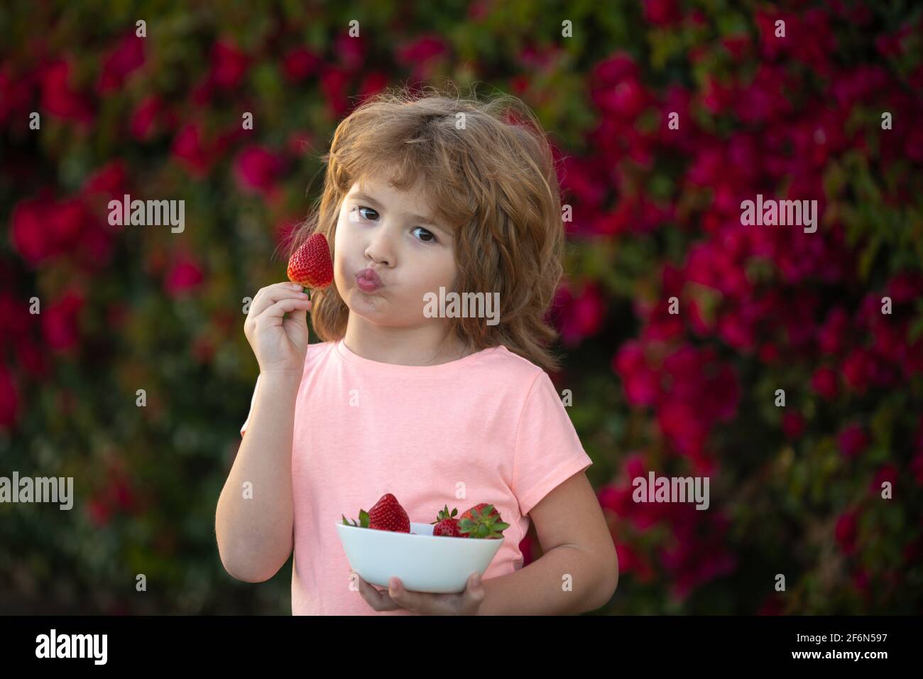 Kids funny face. Cute child eating strawberries. Stock Photo