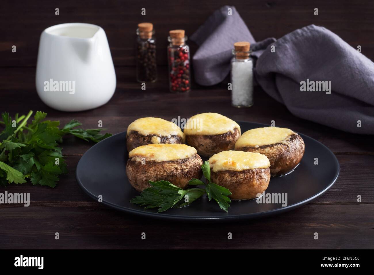 Baked mushrooms stuffed with cheese and herbs on a black plate. wooden background Stock Photo