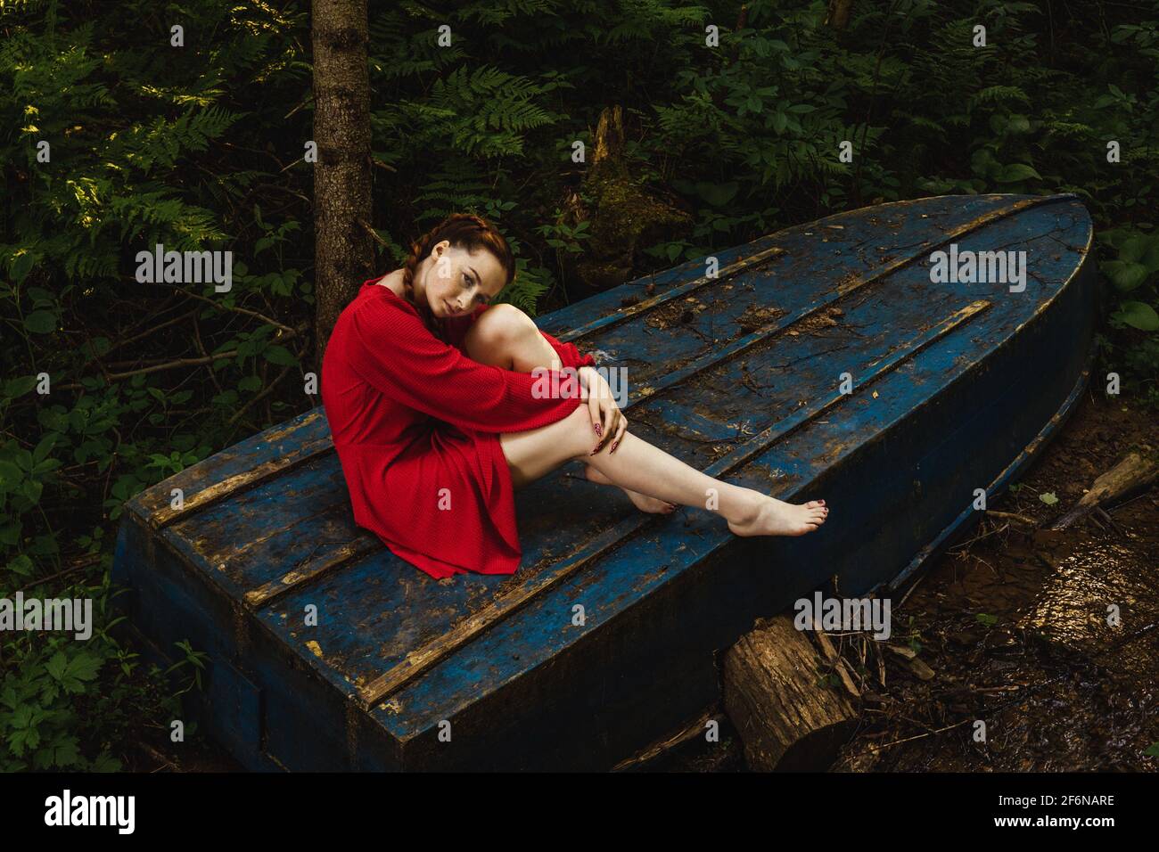 The young woman in red dress sitting on blue boat in forest Stock Photo ...