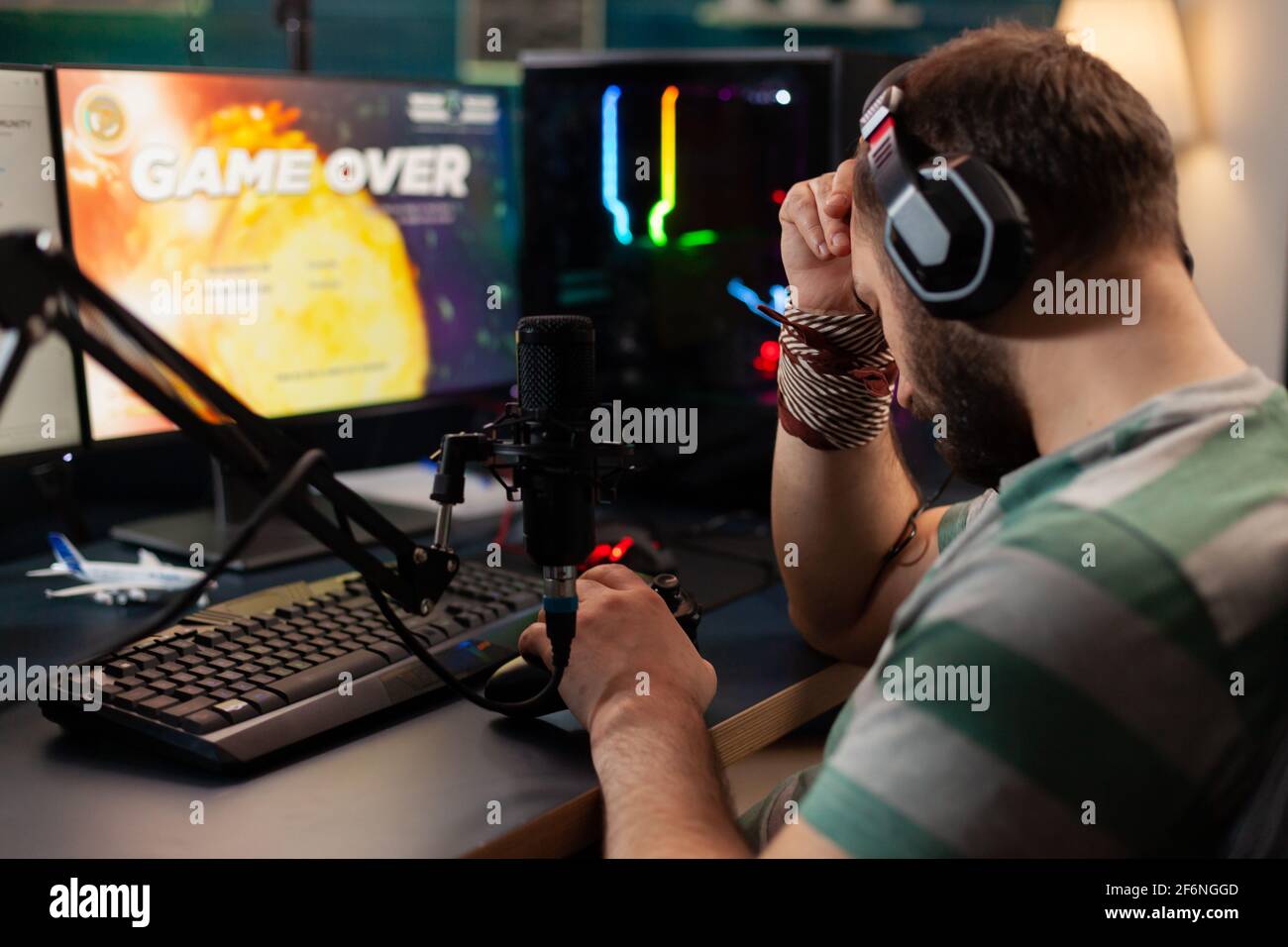 Videogame streamer losing videogame competition while wearing professional headset. Defeated gamer using modern controller for online tournament late at night in gaming room Stock Photo