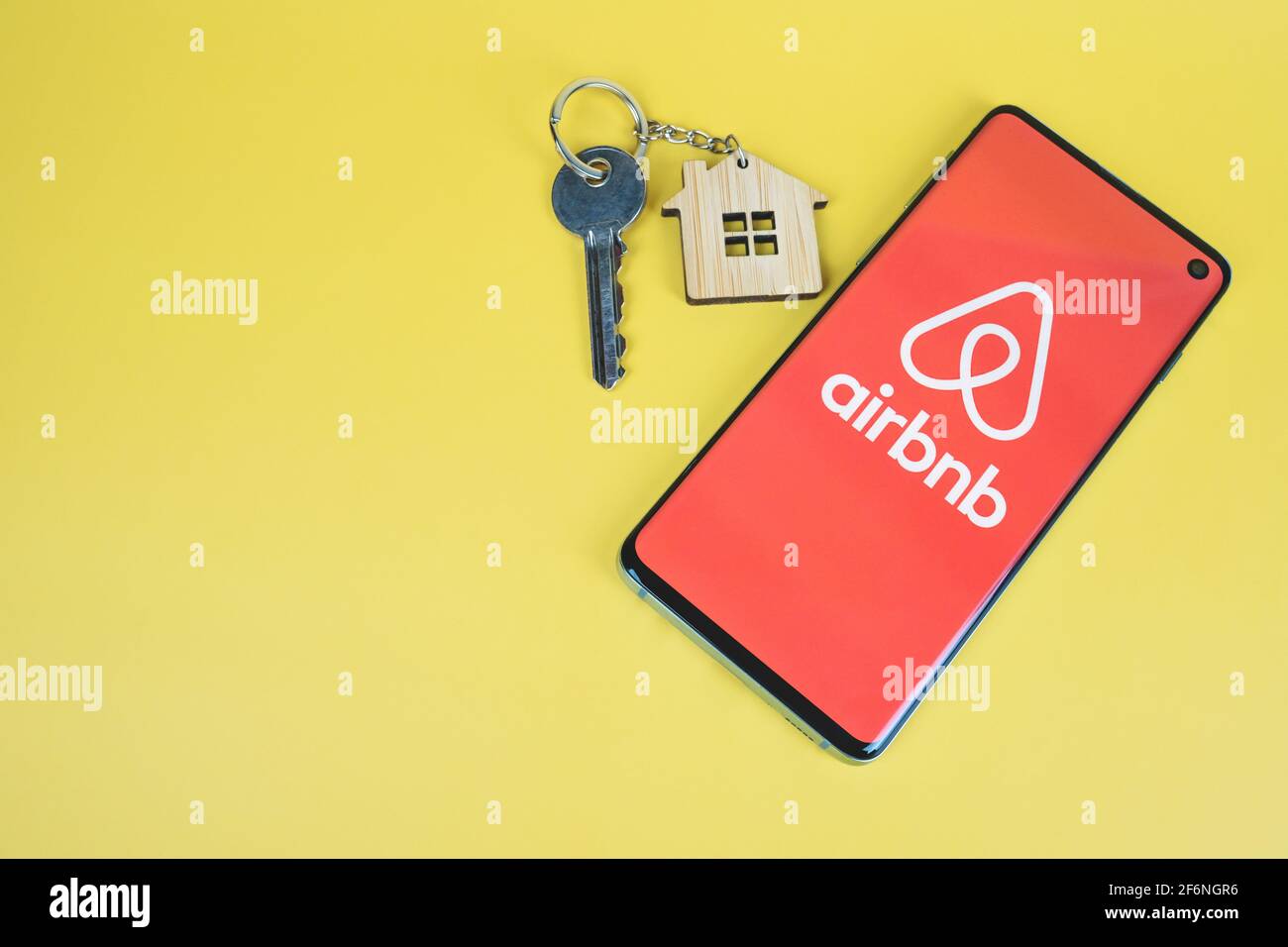 SWANSEA, UK - MARCH 31, 2021: Airbnb app logo displayed on smartphone, home key with house keyring on yellow background with copy space Stock Photo