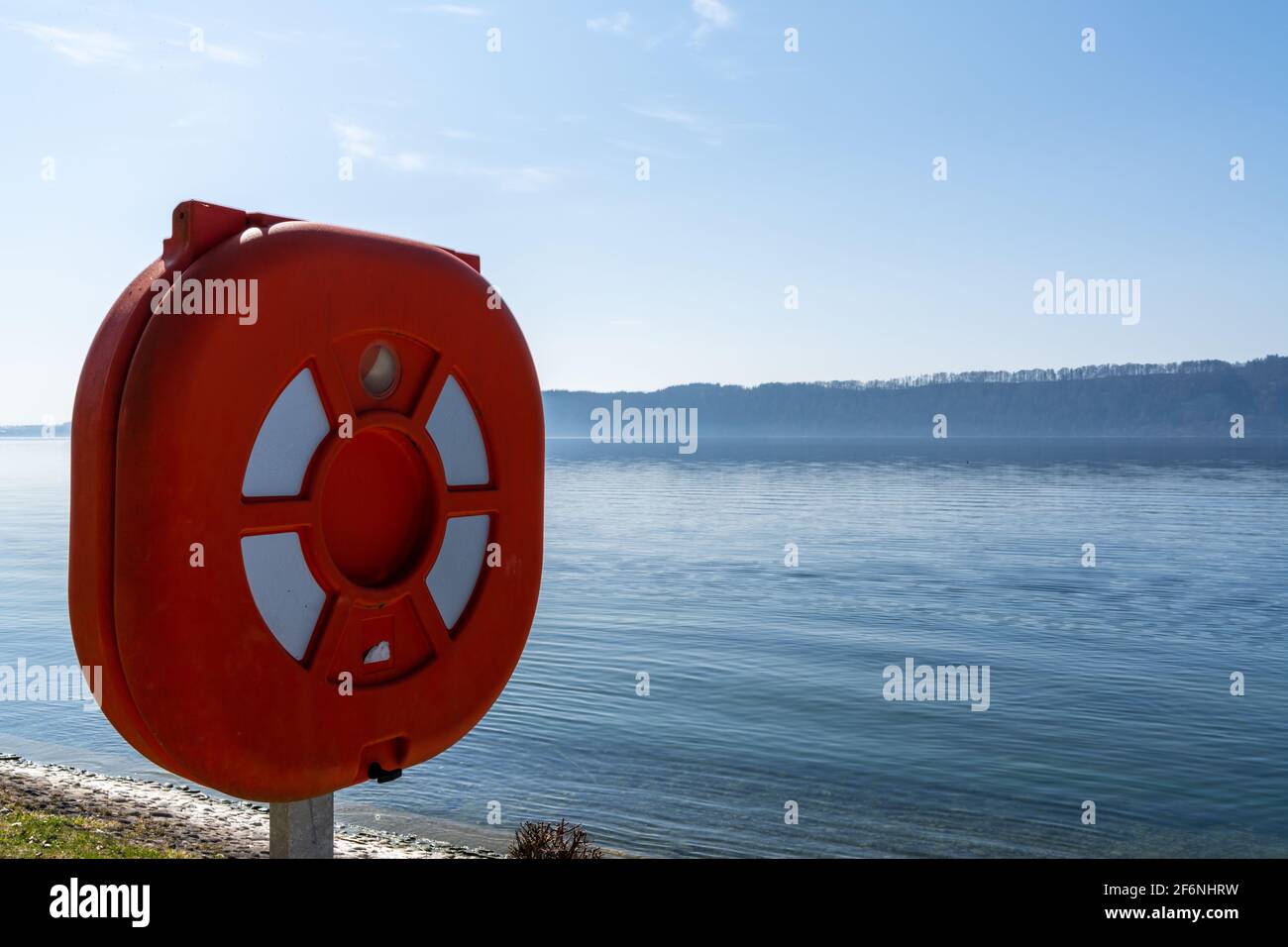 Red rescue ring and station on the shores of a calm blue lake Stock Photo